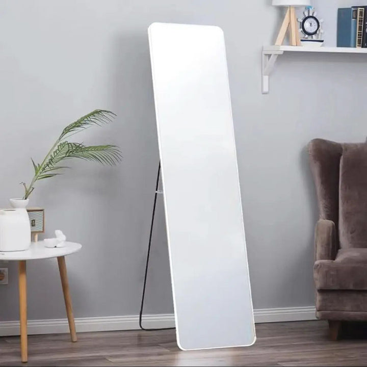 White standing mirror leaning against a gray wall in a room with a sofa and small table.
