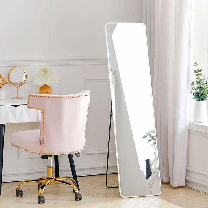 Full-length mirror leaning against a wall in a room with a pink chair and desk.