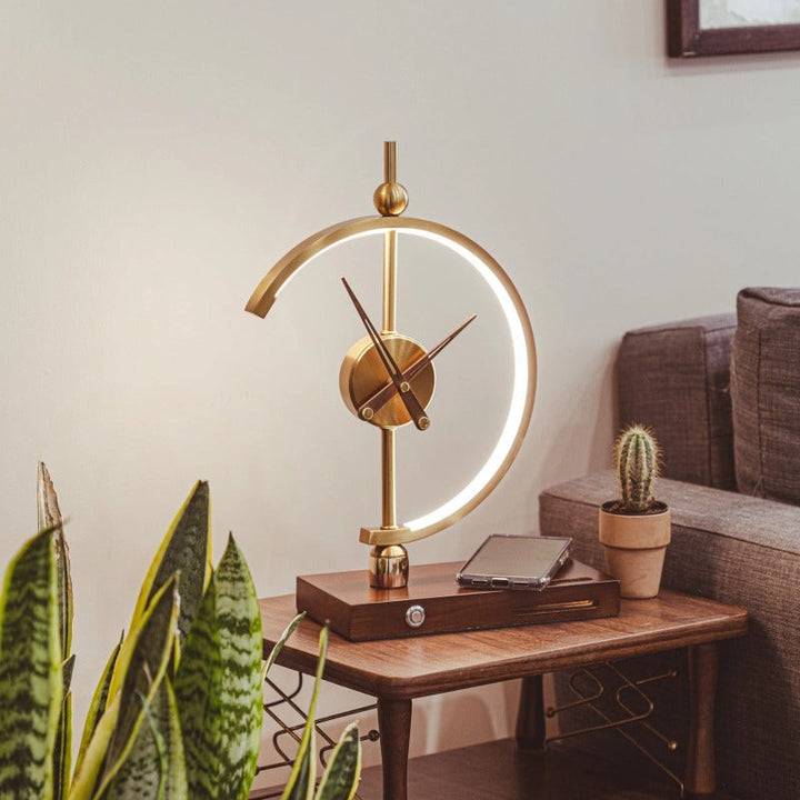 Gold LED lamp clock on wooden base with wireless charging, styled in a living room corner.
