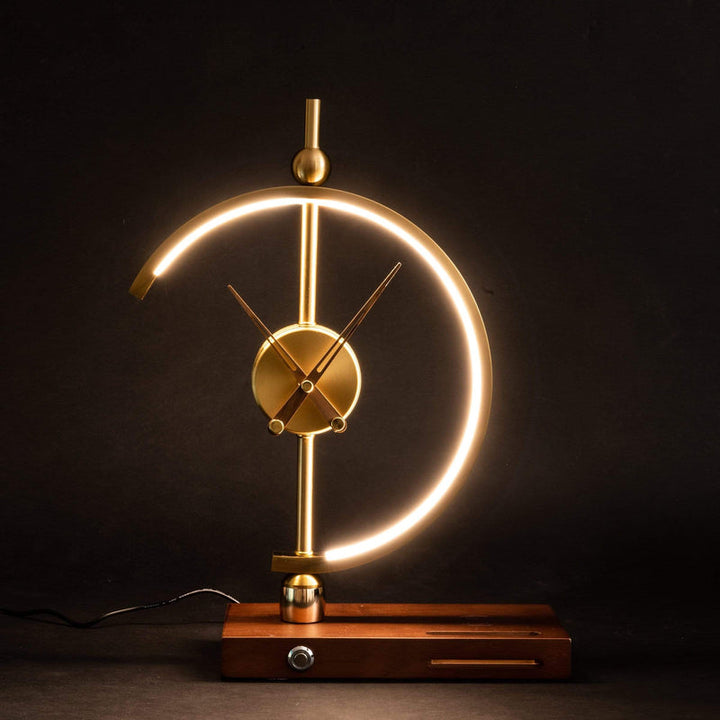 Gold LED lamp clock illuminated on wooden base against a dark backdrop.