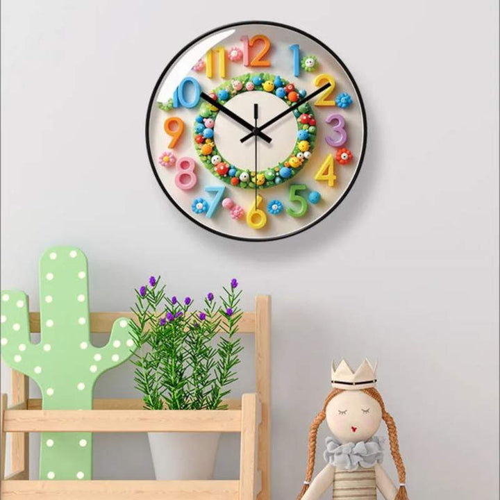 Cartoon wall clock with colourful numbers mounted on a child’s room wall above toys and plants.