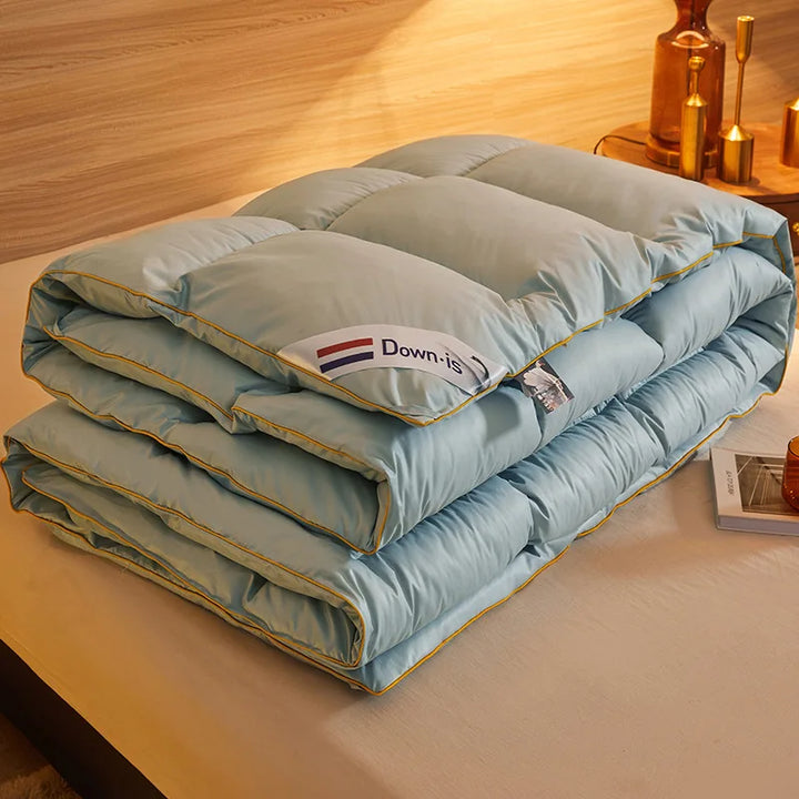 Light blue goose down comforter folded flat on a bed showing smooth quilted stitching and yellow piping.