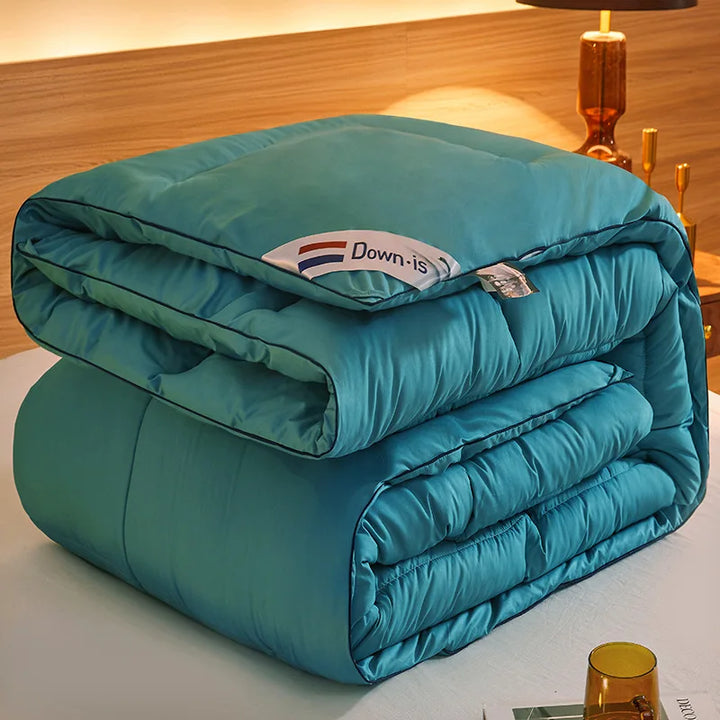 Teal goose down comforter folded thickly with smooth quilted padding and contrasting piping.