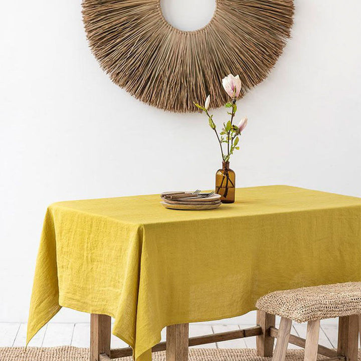 mustard Linen tablecloth on a table with a vase of flowers and decorative mirror on the wall.