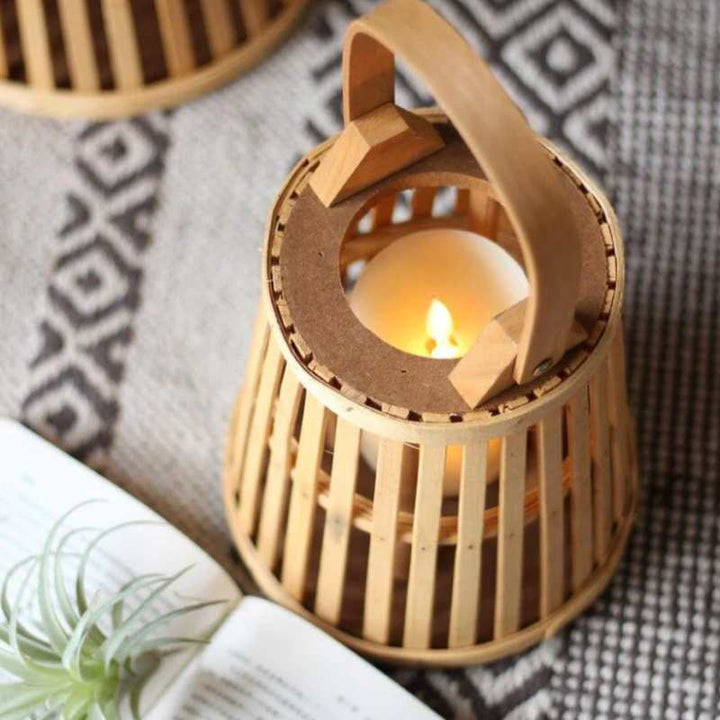 Close-up of small bamboo lantern with glowing candle on textured rug and open book