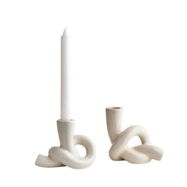 Two white ceramic candle holders with a single candle on a white background