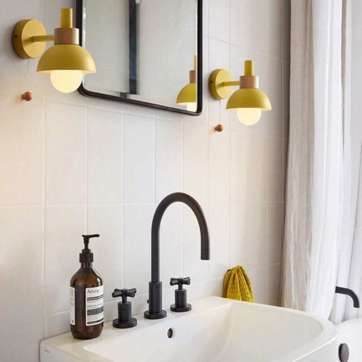 Yellow pastel wall sconces mounted above a sink with green tiles for soft bathroom lighting.