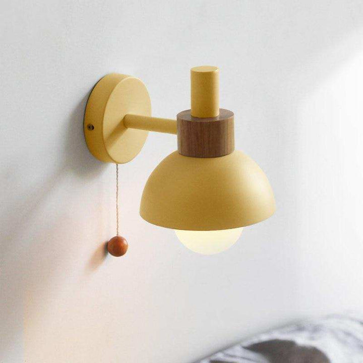 Yellow metal and wood wall light glowing warmly beside a bed in Scandinavian minimalist design.