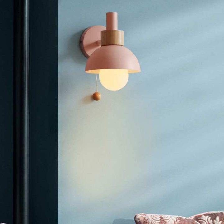 Pink pastel wall lamp with wood accent and globe bulb illuminating a soft blue wall.
