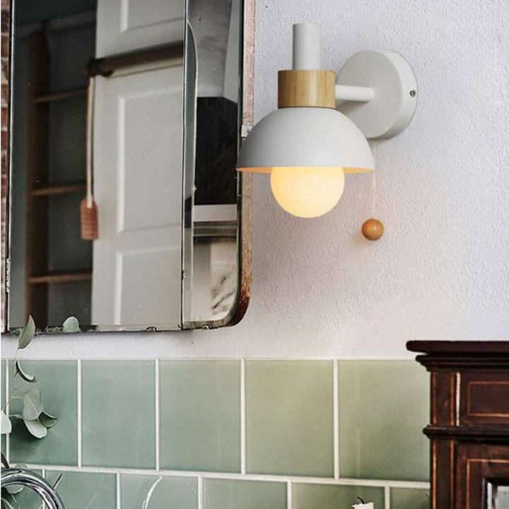 White wall light with natural wood accent and globe bulb beside a mirror in a modern bathroom.