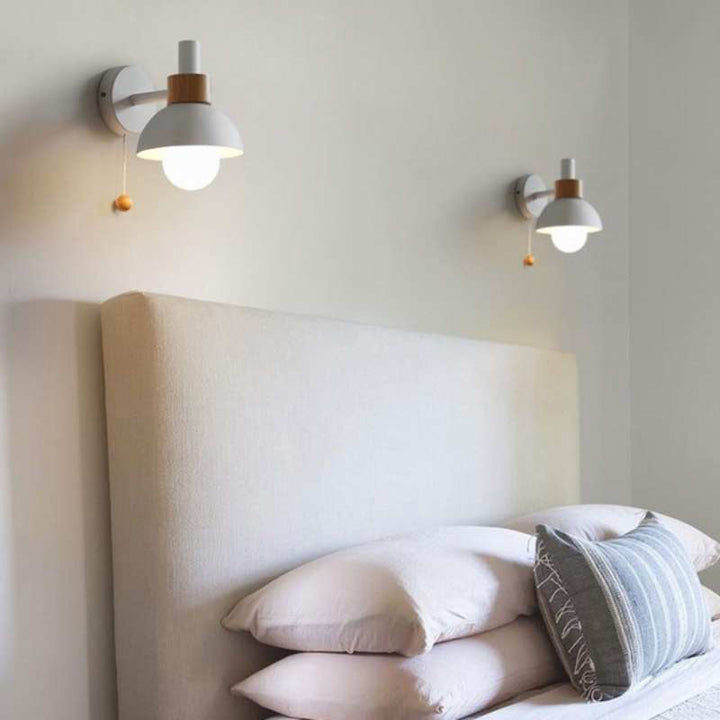 Pair of white wall sconces with wood detail mounted above a beige bedhead for soft ambient light.