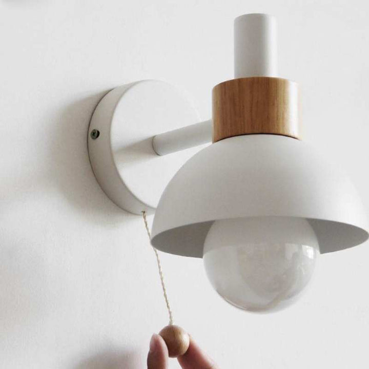 Close-up of white pastel metal wall sconce with wooden detail and pull-chain switch.