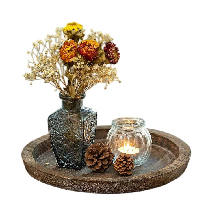 Round wooden tray with glass vase, candle holder, and pinecones in warm rustic home setting
