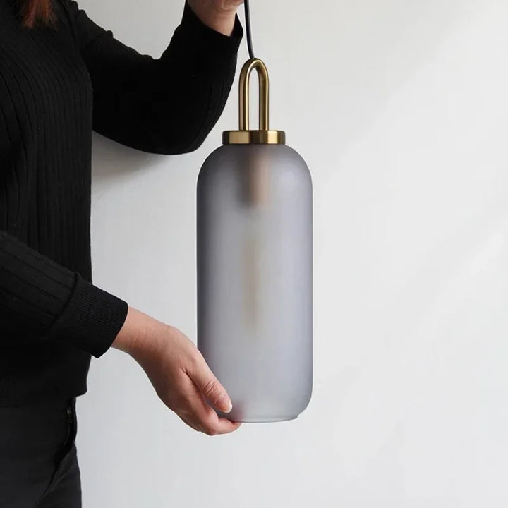 Frosted grey glass pendant light with metal top held by hand against neutral wall