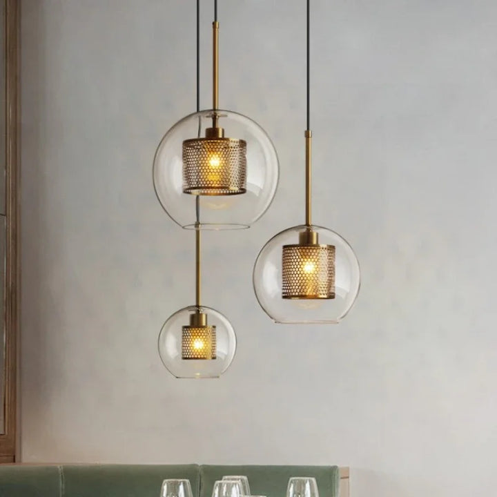 Three round glass pendant lights with metal mesh diffusers hanging above dining table