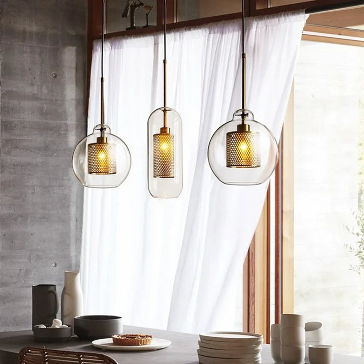 Set of three glass pendant lights with metal mesh shades hanging above modern dining table