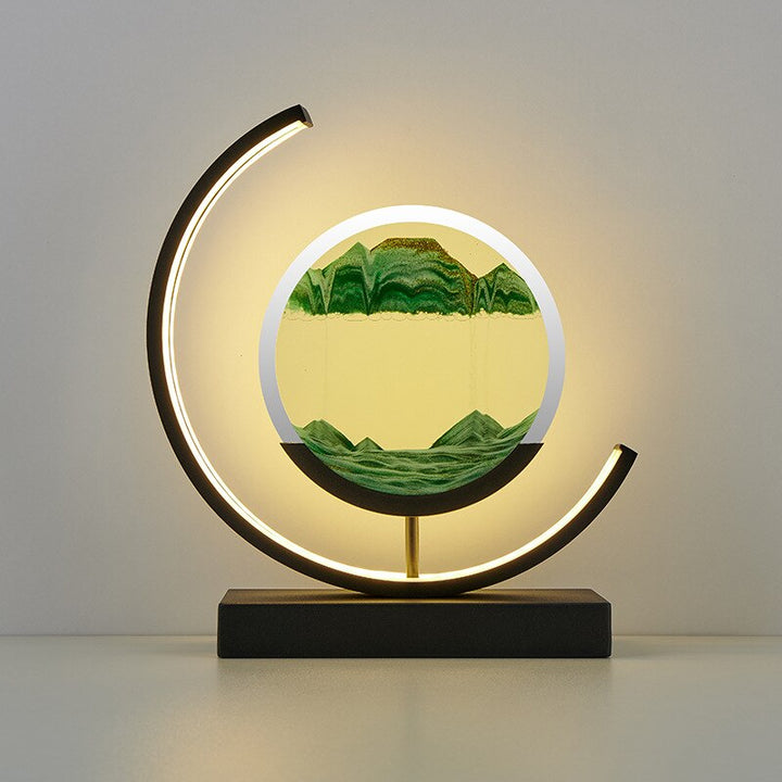Crescent-frame quicksand table lamp with green sand art in a round PMMA display on black base.
