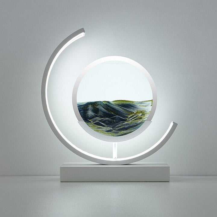 White crescent-frame quicksand table lamp featuring green layered sand art on white base.