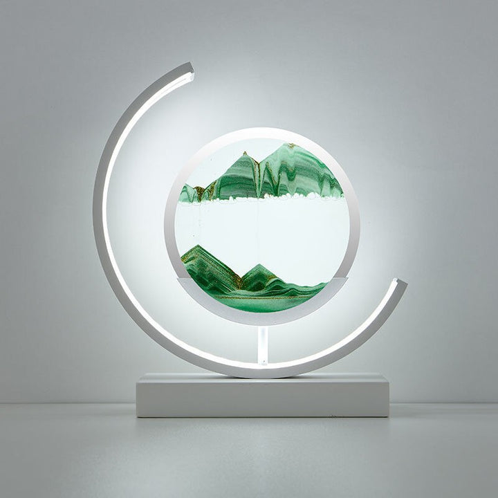 White crescent-frame quicksand lamp with green sand dunes in a round PMMA disc.