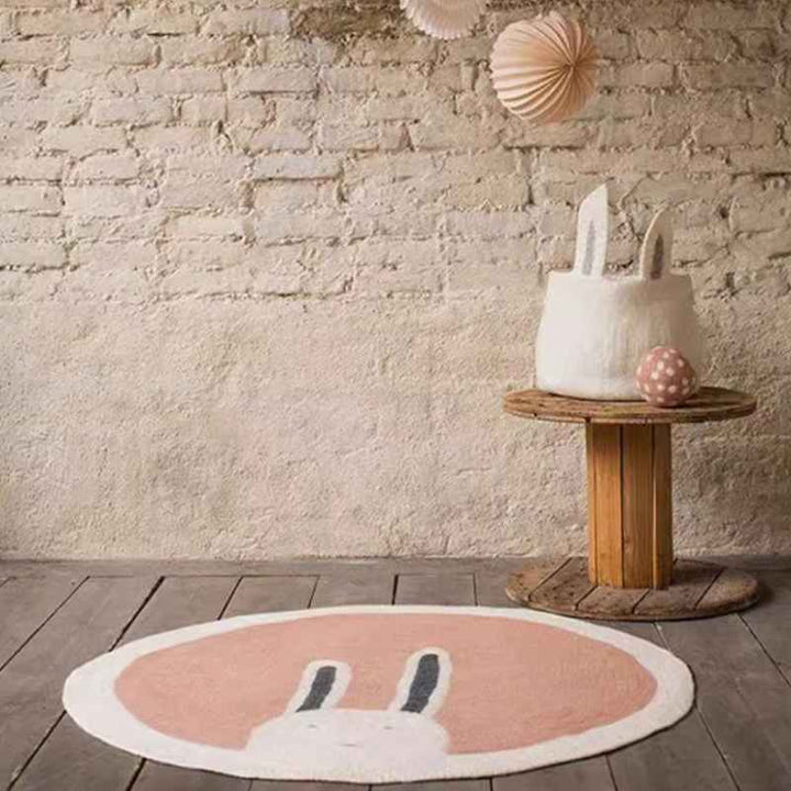 Blush pink round rug with bunny design styled in rustic nursery corner, soft faux cashmere kids’ play mat.