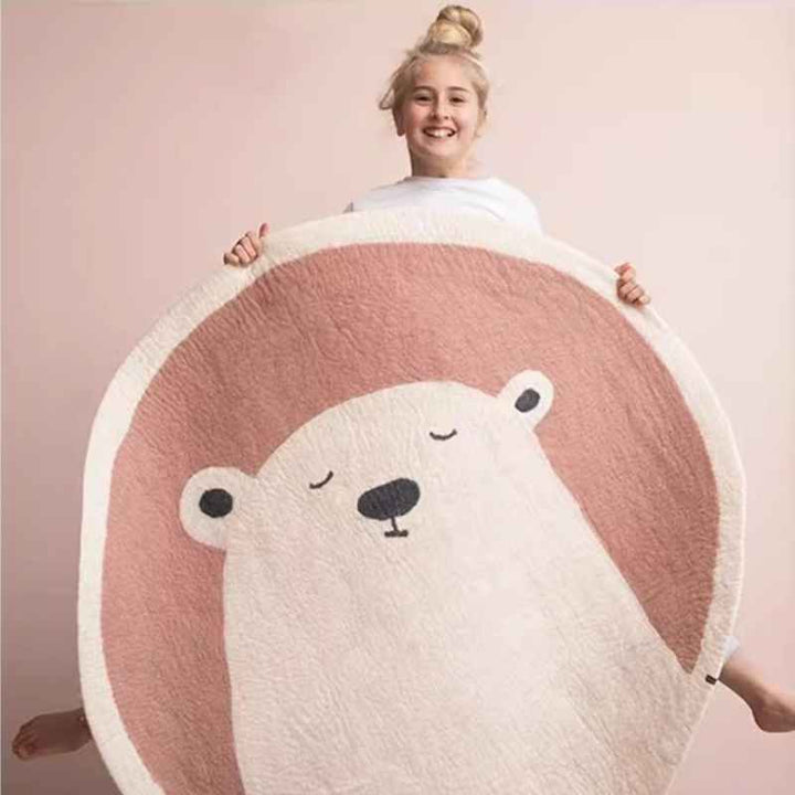 Smiling child holding round polar bear rug in blush tones, ultra-soft faux cashmere nursery carpet.