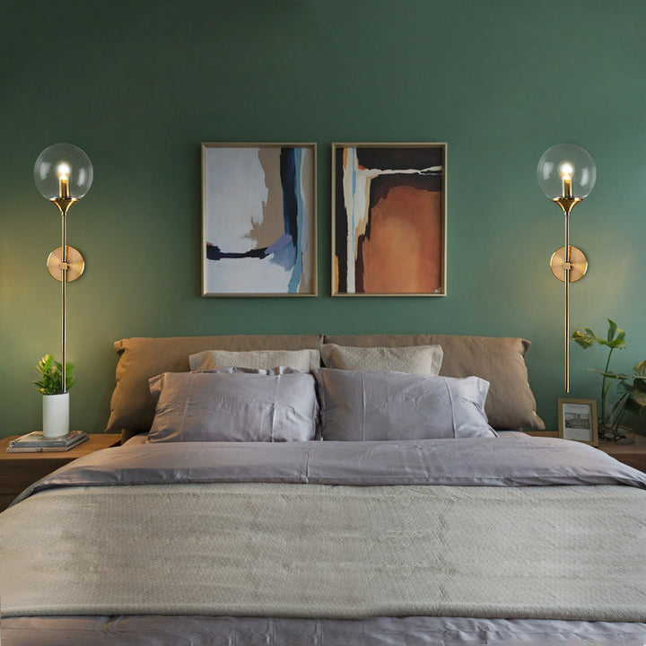 Pair of brass and glass Nordic wall lights beside a bed in a modern green bedroom, creating warm ambient lighting.