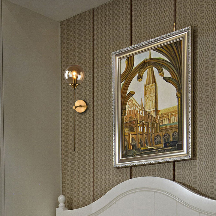 Amber globe wall sconce beside framed artwork, blending classic brass tones with modern elegance.