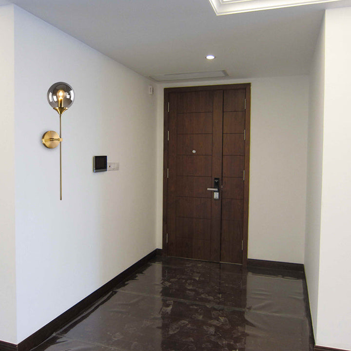 Smoke glass and brass wall sconce beside a wooden entry door, adding a warm modern accent to a minimalist hallway.