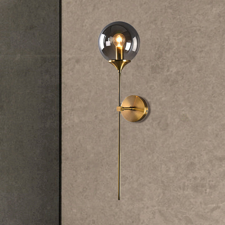 Smoke grey glass wall lamp with brushed brass base on a textured wall, giving a refined Nordic aesthetic.