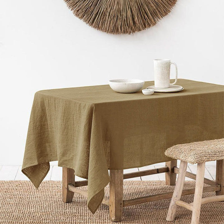 Table with a warm brown linen tablecloth, white bowl, mug, and plates on a neutral background