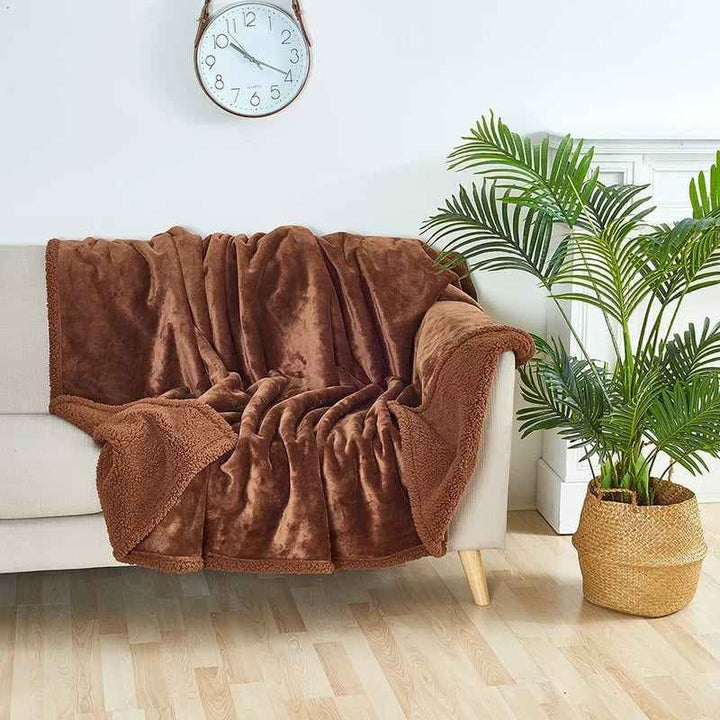 Brown waterproof sherpa blanket draped on beige sofa in bright Scandinavian living room.