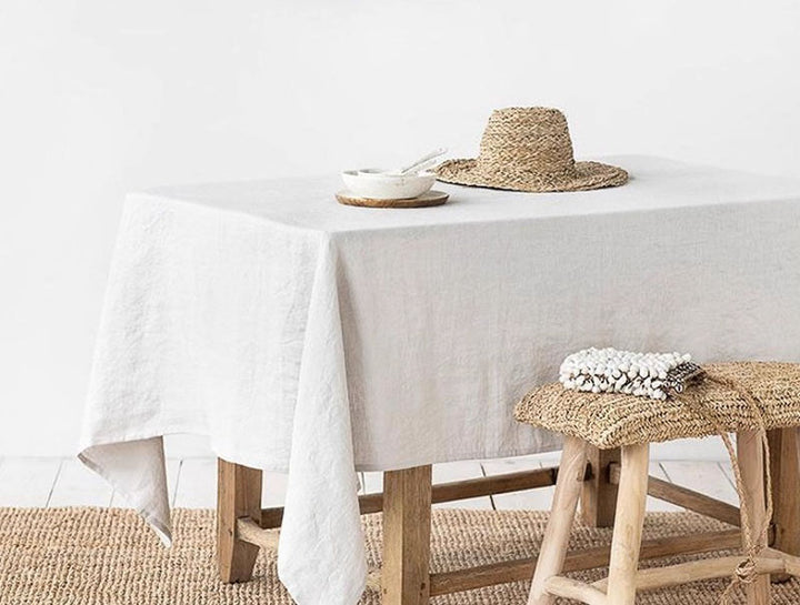 Table setting with a hat, bowl, and towel on a white linen tablecloth.