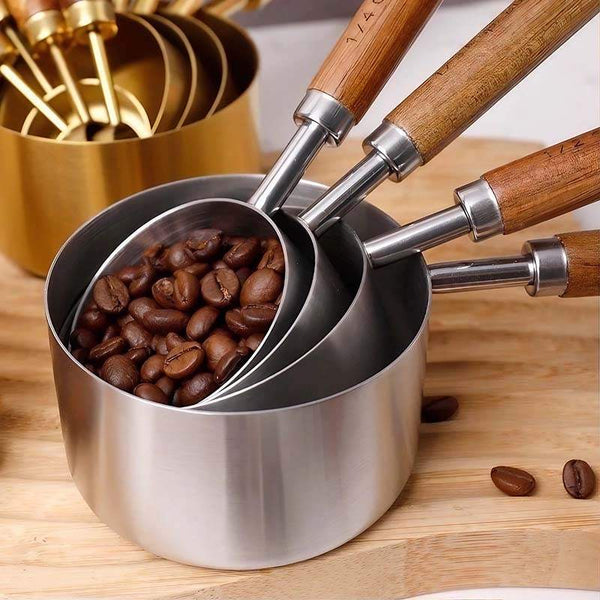 Stainless steel measuring cups with wooden handles filled with coffee beans on wooden surface