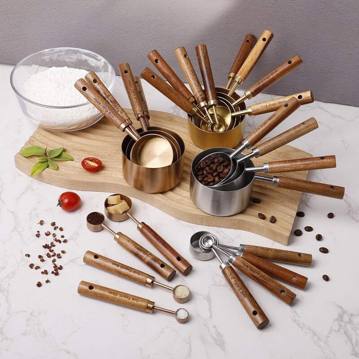 Complete set of gold and silver measuring cups and spoons with wooden handles on marble counter